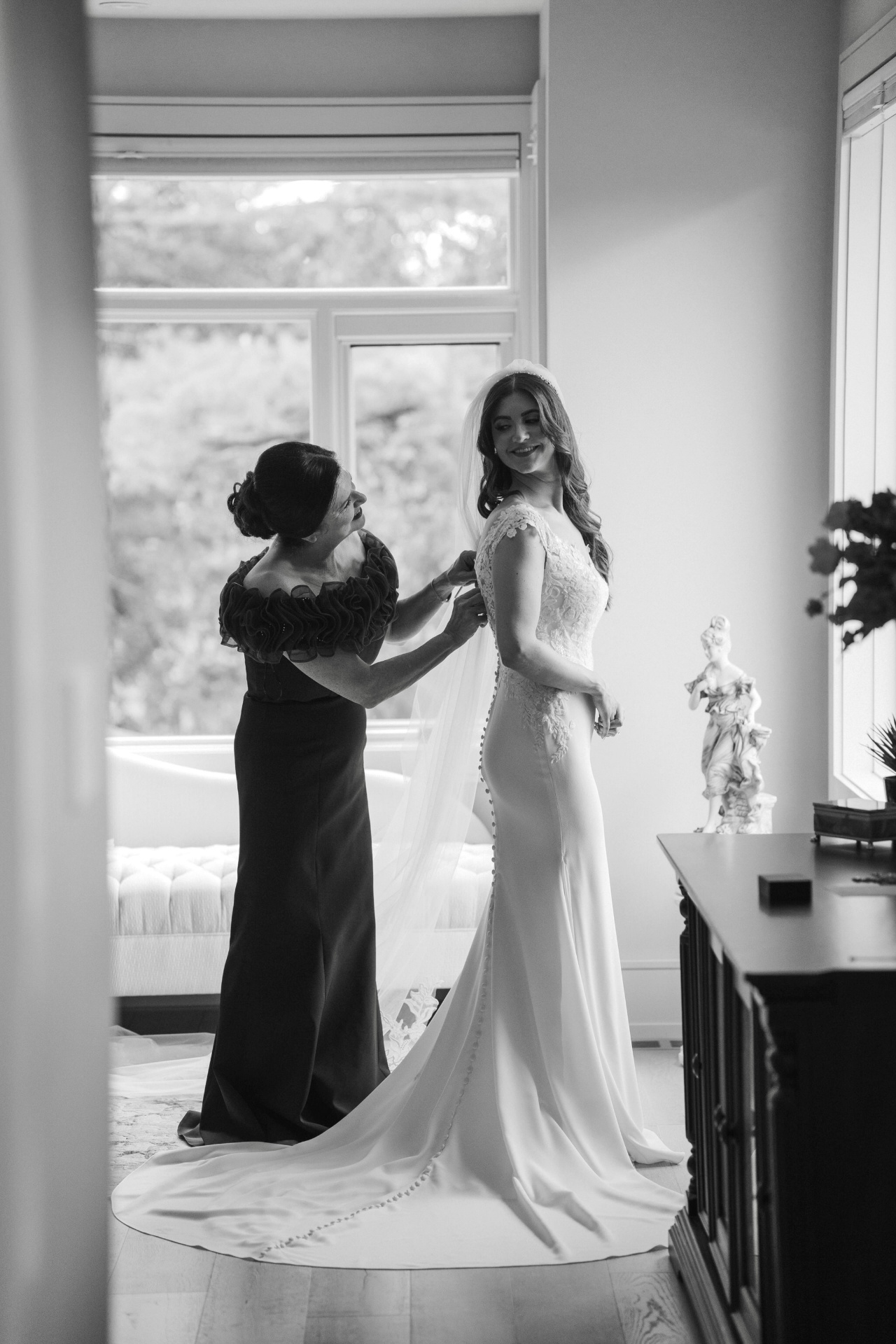 Mother helping bride into her gown in black and white
