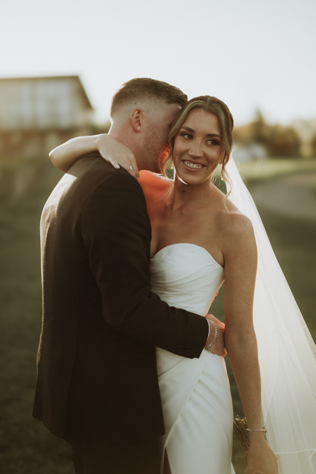 Bride laughing into groom's shoulder in warm light